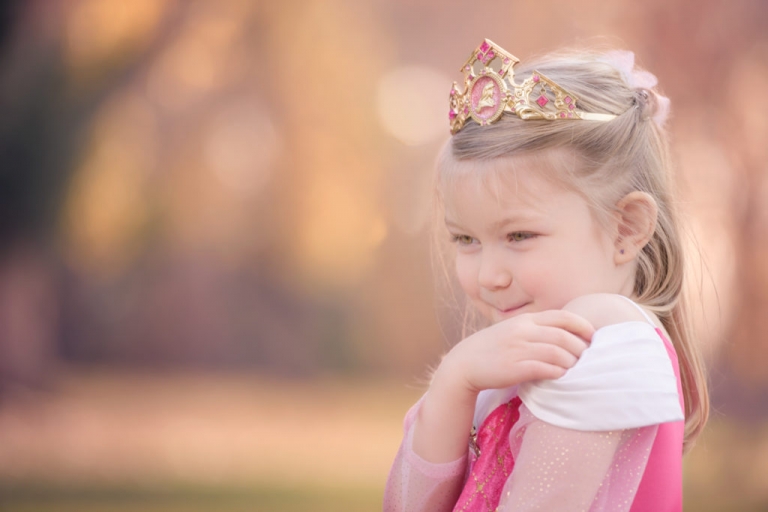 little girl laughing into her hand wearing princess aurora dress