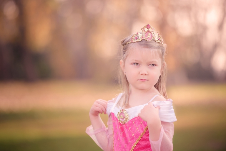 Little girl wearing princess dress touching her hands to her shoulders and looking off