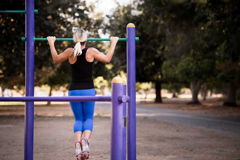 woman at park doing chin ups on exercise equipment